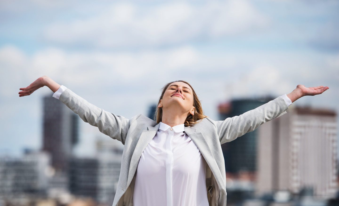 Happy young businesswoman outside with her arms in the air