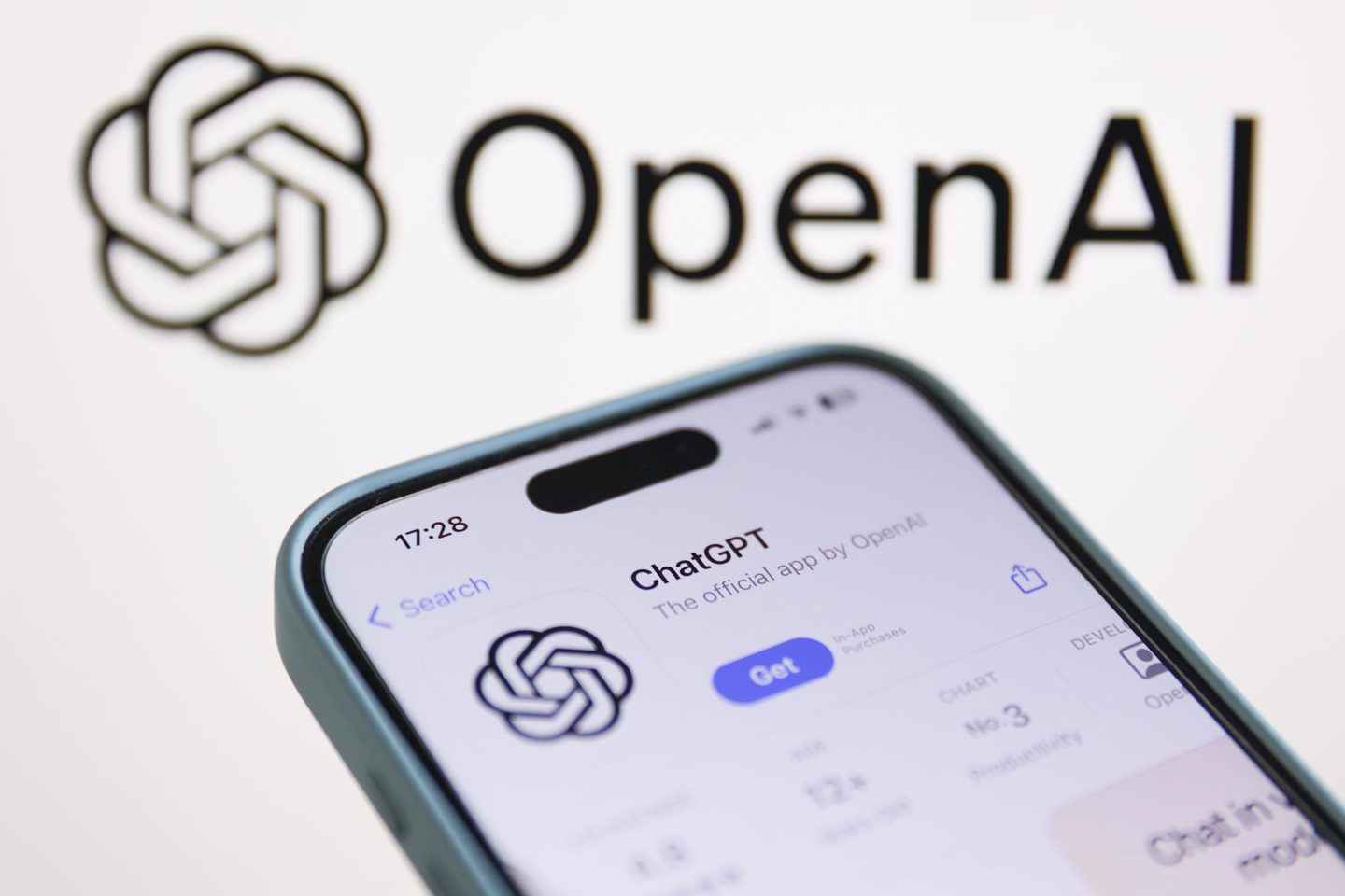 Phone shows the ChatGPT app in the app score, with OpenAI's logo on a screen behind the phone.
