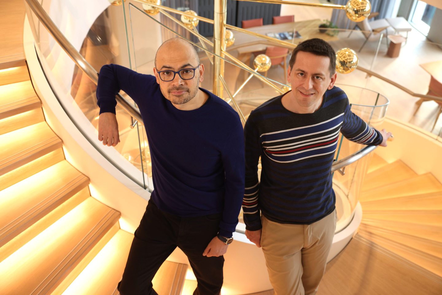 Google DeepMind cofounder and CEO Demis Hassabis (left) and Google DeepMind senior researcher John Jumper stand together on a spiral staircase in DeepMind's London offices.