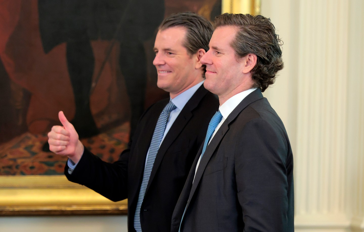 Two men in suits smile in front of a painting