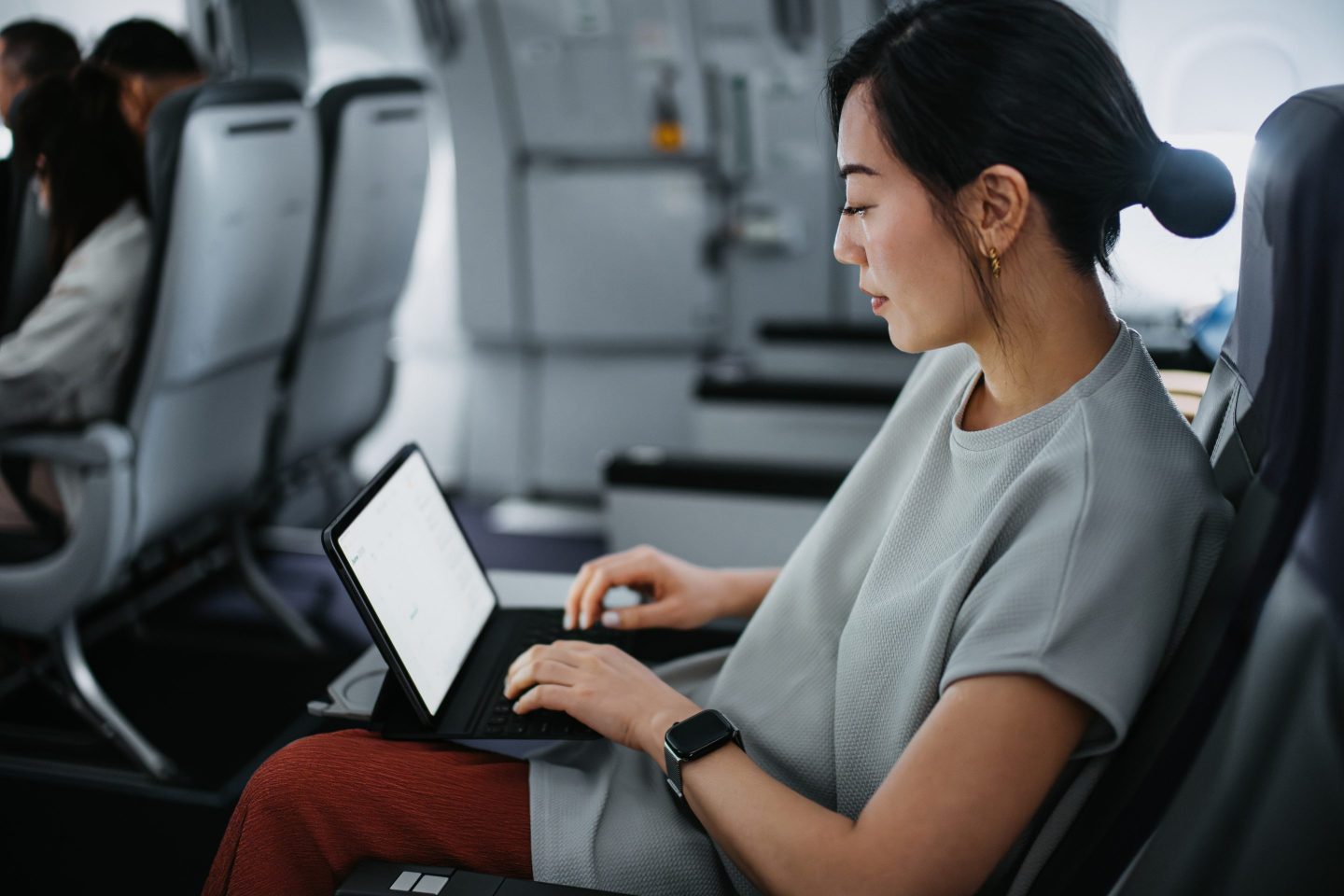 An Asian woman typing on her laptop while sitting on an airplane