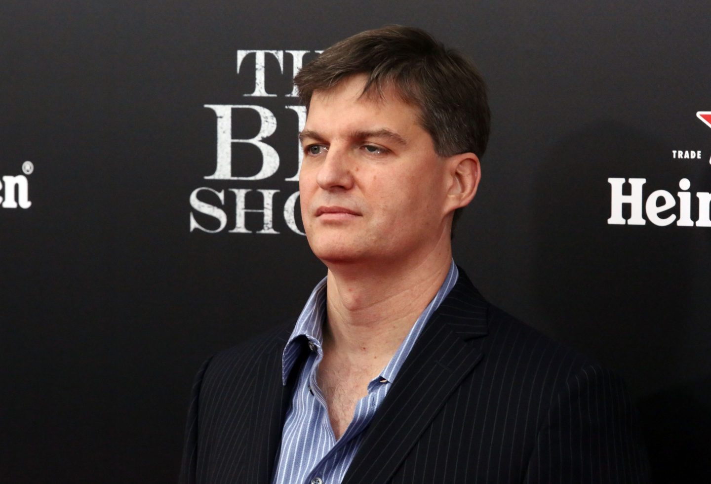 Michael Burry looks to the side. He is standing in front of a background with "The Big Short" printed on it.