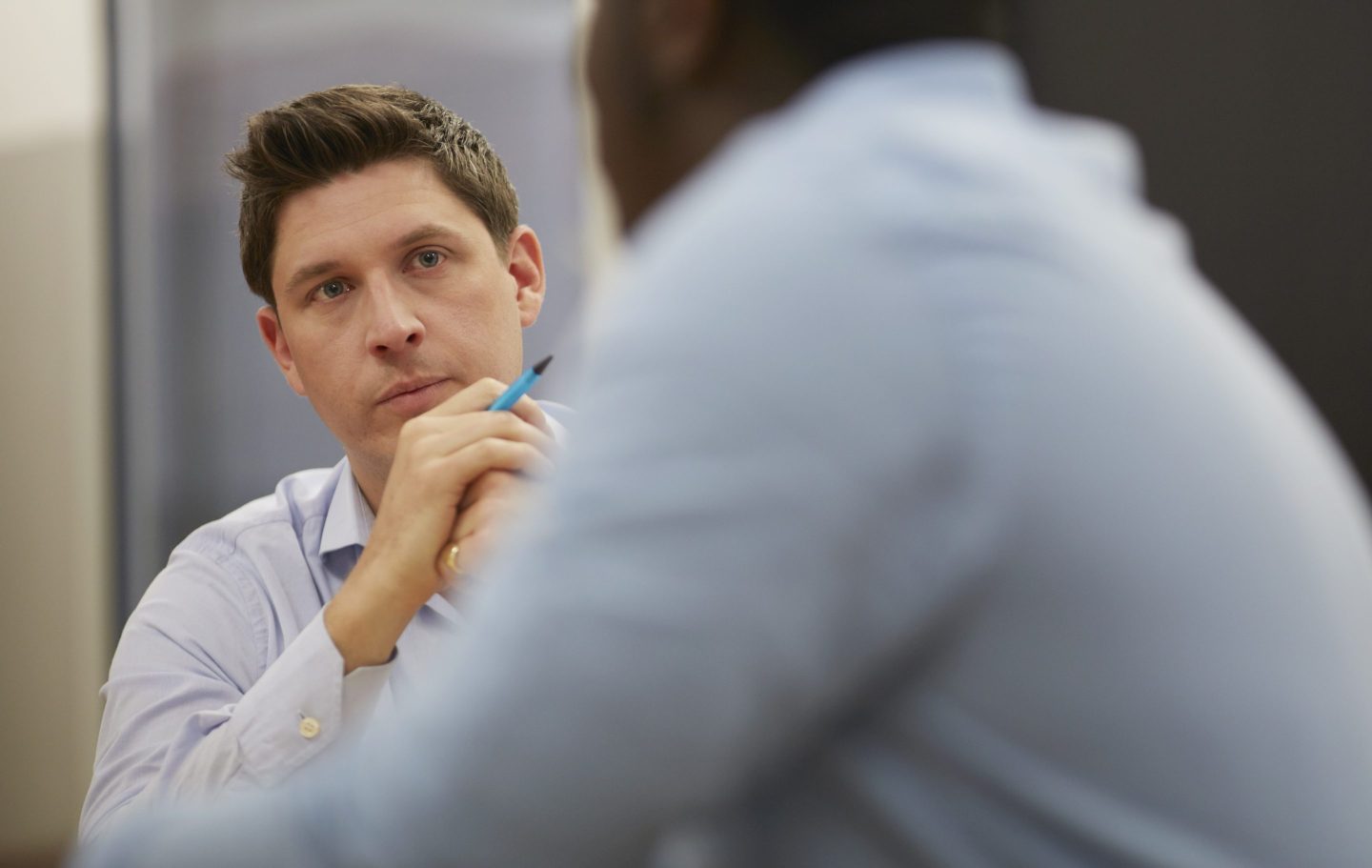 A white man listens to another man in a meeting
