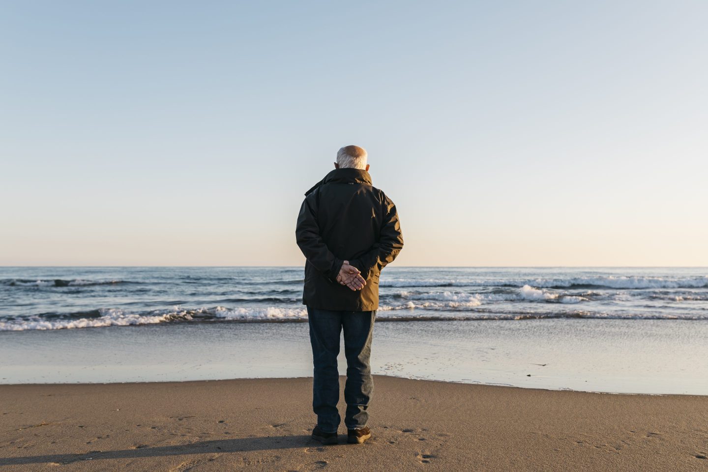 A man alone on a beach wearing a coat, his back to the camera